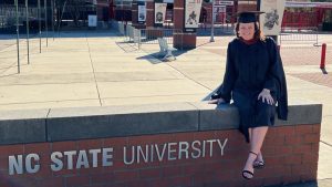 Danielle Morrin sits on a brick wall outside of Carter-Finley Stadium on graduation day.